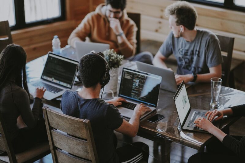 five people at table with laptops