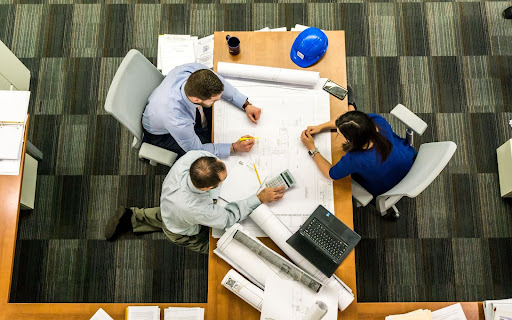 three people sitting around a table looking at plans