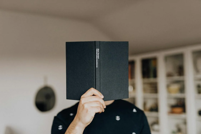 man holding book in front of face